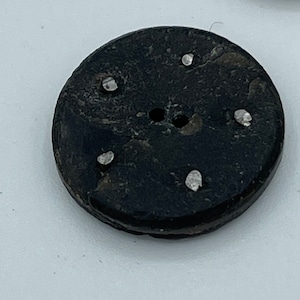 May include: A black round button with five white dots around the center hole.