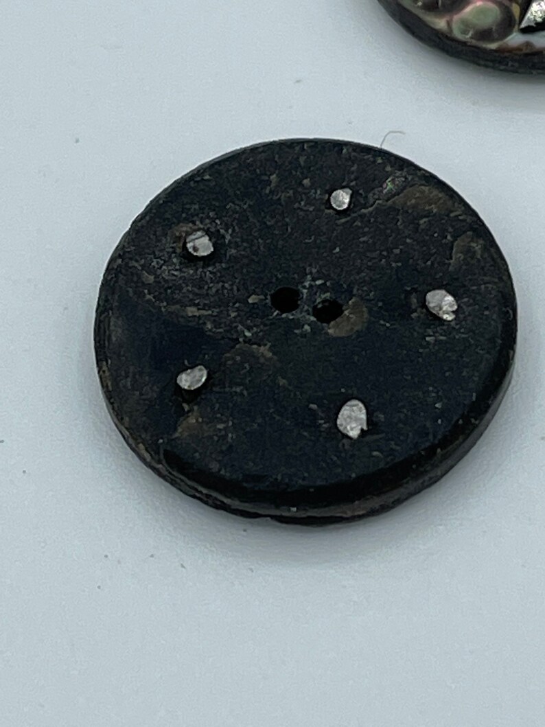 May include: A black round button with five white dots around the center hole.