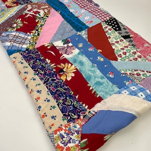 May include: A patchwork quilt made from various colorful fabrics, including floral prints, stripes, and geometric patterns. The quilt is folded in half and has a rustic, vintage aesthetic.