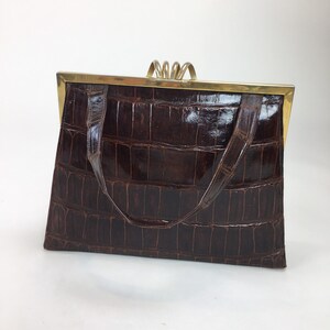 May include: A brown crocodile-embossed leather handbag with a gold-toned clasp and handle.