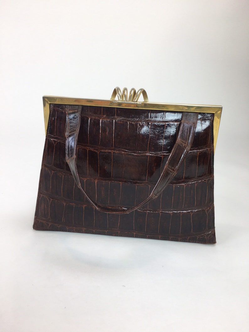 May include: A brown crocodile-embossed leather handbag with a gold-toned clasp and handle.