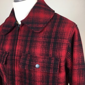 May include: A red and black plaid jacket with a full zipper closure and a large collar. The jacket has two front pockets with a button closure. The jacket is displayed on a mannequin.