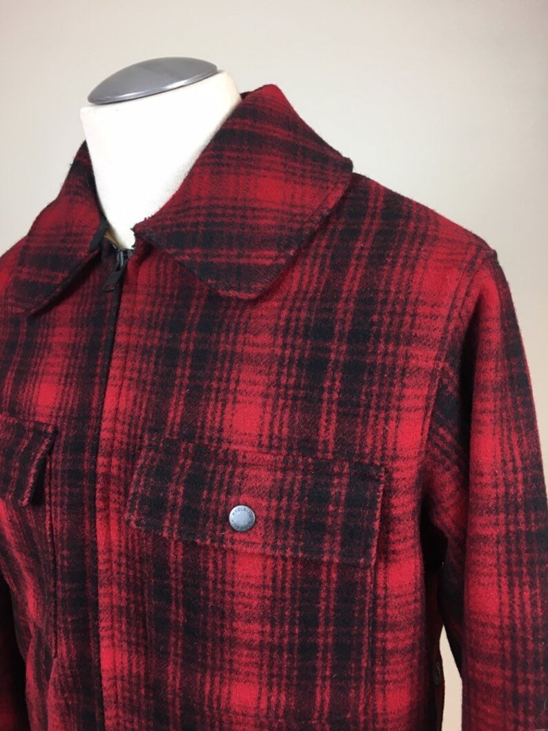 May include: A red and black plaid jacket with a full zipper closure and a large collar. The jacket has two front pockets with a button closure. The jacket is displayed on a mannequin.