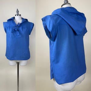Puede incluir: Una camisa azul sin mangas con capucha y lazo en el cuello. La prenda se exhibe en un maniquí, mostrando su diseño y ajuste. La tela parece ser ligera, adecuada para climas cálidos. El diseño es casual.