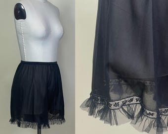 May include: Black vintage slip shorts with a ruffled hem and lace trim. The shorts are displayed on a mannequin. The fabric appears to be a lightweight, semi-sheer material.