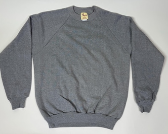 May include: A heather gray sweatshirt with a crew neck and long sleeves. The raglan sleeves extend from the collar to the underarm. The cuffs and hem are ribbed. A small tag is visible near the collar.