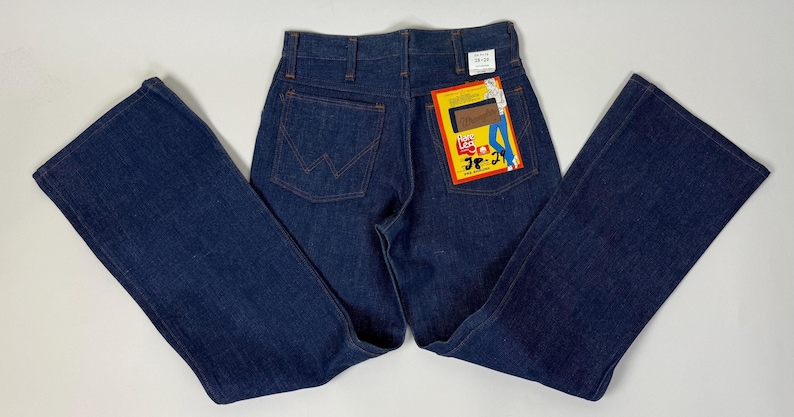 Pode incluir: Cal&ccedil;as de ganga azul escuro com design de perna larga. As cal&ccedil;as de ganga t&ecirc;m um estilo cl&aacute;ssico de cinco bolsos e uma etiqueta Lee Jeans presa ao bolso de tr&aacute;s. As cal&ccedil;as de ganga est&atilde;o colocadas numa superf&iacute;cie branca.