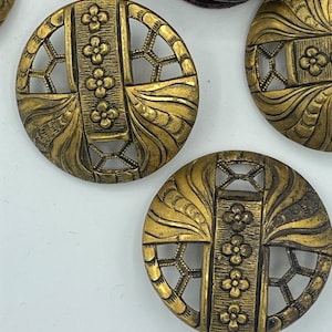 May include: Four gold-toned metal buttons with intricate floral and geometric designs. The buttons have a raised, textured surface and a circular shape.