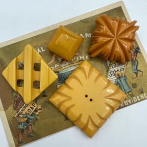 Könnte beinhalten: Vier vintage gelbe und orangefarbene Plastikknöpfe mit verschiedenen Designs. Die Knöpfe befinden sich auf einer Vintage-Werbekarte.