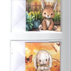 May include: Two greeting cards with watercolour illustrations of rabbits. One card shows a brown rabbit in a garden setting with a fence and watering can. The other depicts a white rabbit with butterflies against an orange sunset.
