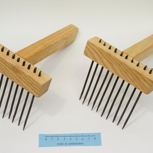 May include: Two wooden wool combs with light brown handles and rows of long, thin, dark metal tines. A blue ruler is positioned between the combs, showing a scale in centimeters with a total length of 8 centimeters for the ruler's markings.