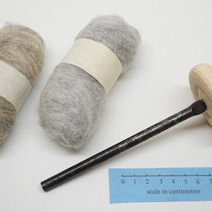 K&ouml;nnte beinhalten: Zwei Wollkn&auml;uel, eines hellbraun und eines grau, mit einem Holzspinnrad mit einer Metallspindel. Die Skala in Zentimetern ist in der rechten unteren Ecke des Bildes sichtbar.