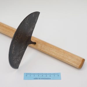 May include: A gardening tool with a curved, metal blade and a wooden handle. The blade is approximately 20 cm long and has a textured surface. The handle is about 46 cm long and is made of light-coloured wood.
