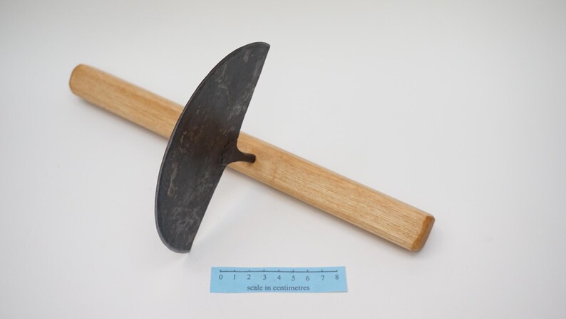 May include: A gardening tool with a curved, metal blade and a wooden handle. The blade is approximately 20 cm long and has a textured surface. The handle is about 46 cm long and is made of light-coloured wood.
