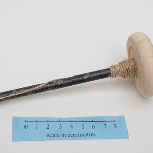 K&ouml;nnte beinhalten: Ein Holzspinnrad mit einer Metallspindel und einer L&auml;nge von Garn, das um sie gewickelt ist. Die Spindel ist etwa 20 cm lang.