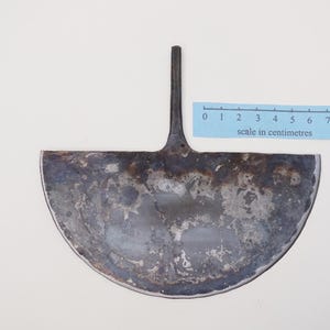 May include: A metal gardening tool shaped like a half-circle with a long handle. The tool is rusty and has a scale in centimetres printed on a blue strip below it.