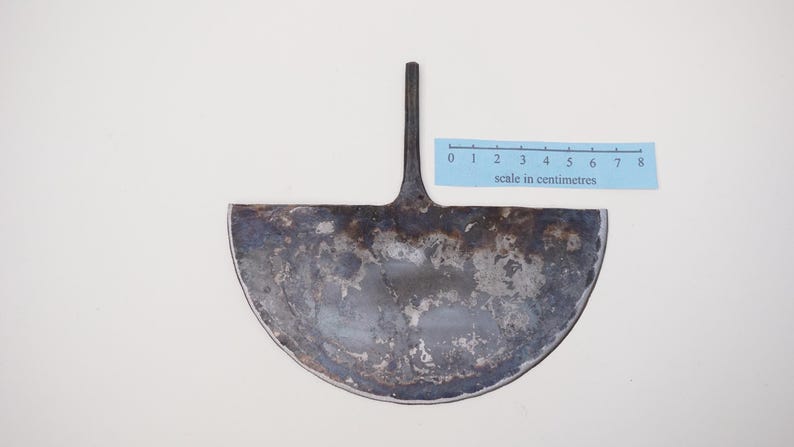May include: A metal gardening tool shaped like a half-circle with a long handle. The tool is rusty and has a scale in centimetres printed on a blue strip below it.