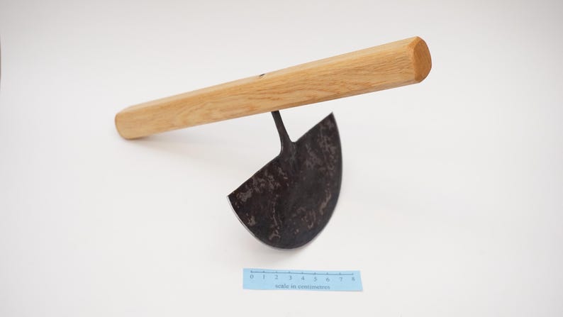 May include: A gardening tool with a wooden handle and a curved, metal blade. The blade is dark grey and has a rough texture. The handle is light brown and has a smooth finish.