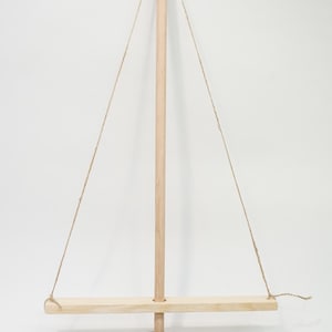 Op de afbeelding: Een houten vuurboor met een bruin klei vuurplank. De boor is met een touw aan een houten balk bevestigd. De balk hangt met twee touwen aan de boor. Onderaan de afbeelding is een liniaal te zien met de tekst "schaal in centimeters".