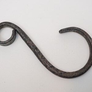May include: A handcrafted, dark gray metal hook with a distinctive S-shape. The hook features a circular loop on one end and a curved, open hook on the other. The metal has a textured, aged appearance, suggesting a rustic or vintage style.