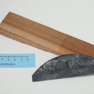 Può includere: Primo piano di una tavola di legno con un righello che misura 8 centimetri. Uno strumento in metallo con una lama curva è appoggiato sulla tavola.