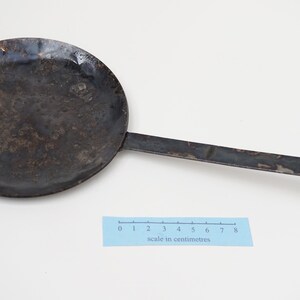 Puede incluir: Una sart&eacute;n de metal negro con un mango largo. La sart&eacute;n tiene un di&aacute;metro de unos 18 cm y un extremo redondeado en el mango. La sart&eacute;n est&aacute; ligeramente desgastada y tiene algunas manchas de &oacute;xido.