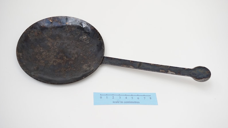 Puede incluir: Una sart&eacute;n de metal negro con un mango largo. La sart&eacute;n tiene un di&aacute;metro de unos 18 cm y un extremo redondeado en el mango. La sart&eacute;n est&aacute; ligeramente desgastada y tiene algunas manchas de &oacute;xido.
