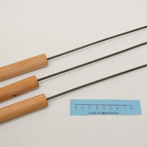 Pu&ograve; includere: Tre strumenti in metallo con manico in legno e un gancio piegato all'estremit&agrave;. Gli strumenti sono disposti su una superficie bianca con un righello che misura 8 centimetri.