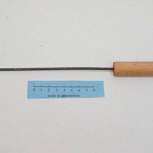 Pu&ograve; includere: Uno strumento di metallo lungo e sottile con un manico di legno. La parte metallica &egrave; piegata ad angolo retto vicino al manico. Lo strumento &egrave; lungo circa 20 cm.