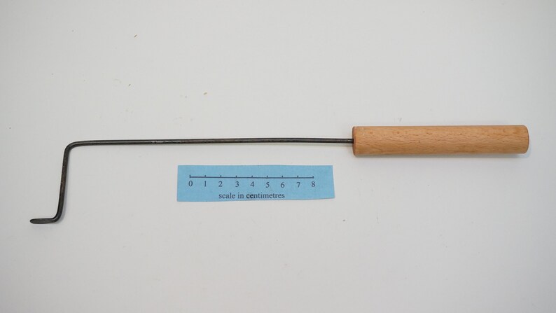 Pu&ograve; includere: Uno strumento di metallo lungo e sottile con un manico di legno. La parte metallica &egrave; piegata ad angolo retto vicino al manico. Lo strumento &egrave; lungo circa 20 cm.