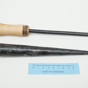 May include: Two tools with wooden handles and metal shafts. The top tool has a long, thin shaft and the bottom tool has a shorter, thicker shaft. A ruler is included for scale, showing the tools are approximately 18 cm and 20 cm long.