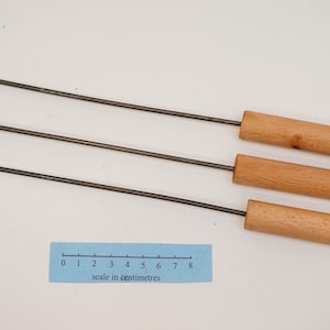 Pu&ograve; includere: Quattro attrezzi per camino in metallo con manici in legno. Gli attrezzi hanno estremit&agrave; di forme diverse, tra cui un gancio, un anello e un'estremit&agrave; piatta. Gli attrezzi sono lunghi 20 cm e sono mostrati su uno sfondo bianco con un righello per la scala.