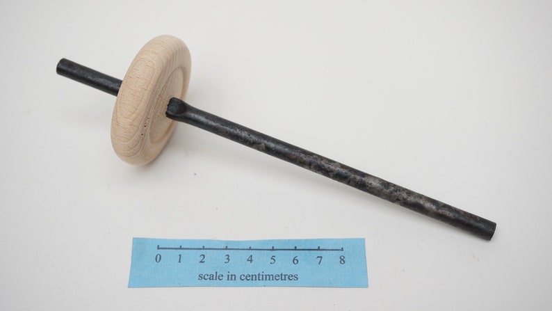 K&ouml;nnte beinhalten: Ein Holzrad, das an einer langen, d&uuml;nnen, schwarzen Metallstange befestigt ist. Die Stange ist etwa 20 cm lang. Ein Lineal ist im Bild zur Skalierung zu sehen.