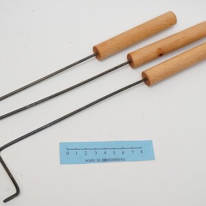 Pu&ograve; includere: Tre strumenti in metallo con manici in legno e un gancio piegato all'estremit&agrave;. Gli strumenti sono disposti su una superficie bianca con un righello che misura 8 centimetri.