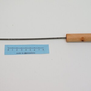 Pu&ograve; includere: Uno strumento di metallo lungo e sottile con un manico di legno. La parte metallica &egrave; piegata ad un angolo di 90 gradi, formando un gancio. Lo strumento &egrave; lungo circa 20 cm.