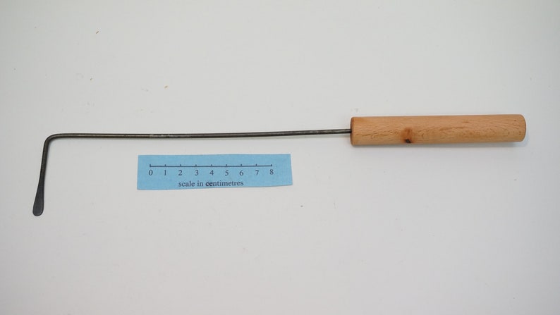 Pu&ograve; includere: Uno strumento di metallo lungo e sottile con un manico di legno. La parte metallica &egrave; piegata ad un angolo di 90 gradi, formando un gancio. Lo strumento &egrave; lungo circa 20 cm.