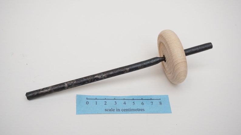 K&ouml;nnte beinhalten: Ein Holzrad mit einer daran befestigten Metallstange. Die Stange ist etwa 20 cm lang. Das Rad hat einen Durchmesser von etwa 5 cm.