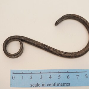 May include: A rustic, dark metal hook with a curved design. The hook is approximately 8 inches long, with a circular loop on one end and a curved hook on the other. The hook is likely for hanging items.