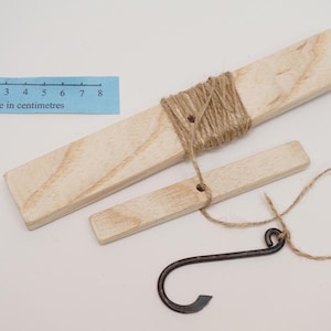 May include: A wooden tool for making cordage, consisting of two wooden pieces and a metal hook. The larger piece is 8 cm long and wrapped with twine. The smaller piece is 6 cm long and has a hole for the twine to pass through. The metal hook is attached to the twine.