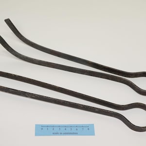 Könnte beinhalten: Zwei dunkelgraue Metallzangen mit einem Griff in Schlaufenform. Jedes Werkzeug besteht aus einem einzigen Stück Metall, das zu einer langen, schmalen Form gebogen ist. Ein blaues Lineal unter den Zangen zeigt eine Skala in Zentimetern bis 8 cm.