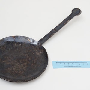 Puede incluir: Una sart&eacute;n de metal negro con un mango largo. La sart&eacute;n tiene un di&aacute;metro de unos 15 cm y un fondo ligeramente redondeado. El mango mide unos 18 cm de largo y tiene un extremo redondeado.