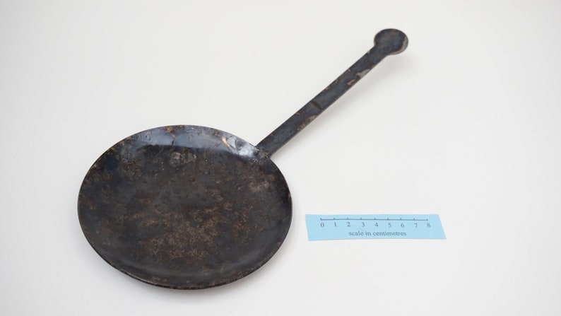 Puede incluir: Una sart&eacute;n de metal negro con un mango largo. La sart&eacute;n tiene un di&aacute;metro de unos 15 cm y un fondo ligeramente redondeado. El mango mide unos 18 cm de largo y tiene un extremo redondeado.