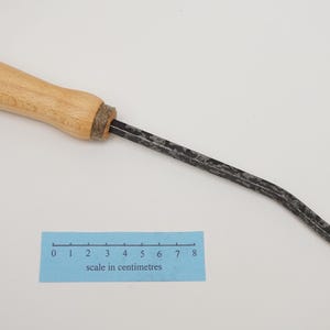 Op de afbeelding: Een zwart metalen gereedschap met een houten handvat en een gebogen mes. Het gereedschap is 20 cm lang en heeft een schaal in centimeters ter referentie.