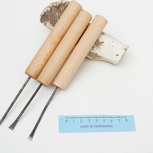 Könnte beinhalten: Drei Werkzeuge mit Holzgriffen und Metallspitzen. Die Werkzeuge liegen auf einer weißen Oberfläche mit einem blauen Lineal, auf dem "Maßstab in Zentimetern" steht und Markierungen von 0 bis 8 vorhanden sind.