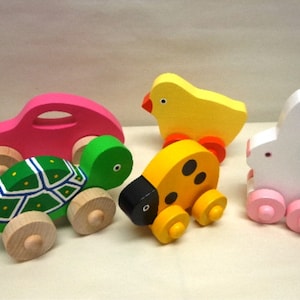 May include: A set of five wooden pull toys. The toys are a pink car, a green turtle, a yellow ladybug, a yellow chick, and a white rabbit. Each toy has wheels and is painted in bright colors.