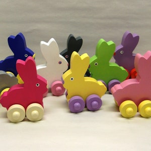 May include: A collection of colorful wooden bunny toys on wheels. The bunnies are painted in various colors, including pink, yellow, green, and blue, with contrasting wheel colors. Each bunny has a simple, rounded design.