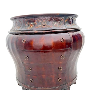 May include: A dark brown wooden chest with four drawers and ornate carvings. The chest has a rounded, almost vase-like shape and sits on four short legs.