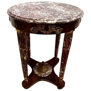 May include: A round, marble-top side table with a dark wood base and gold accents. The table has three legs and a decorative design around the top edge.