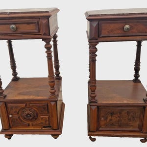 May include: A pair of tall wooden bedside tables featuring a dark brown finish, each with a single top drawer, a lower cabinet door with carved detailing, and four turned spindle legs supporting a flat top surface with a marble-like inlay.