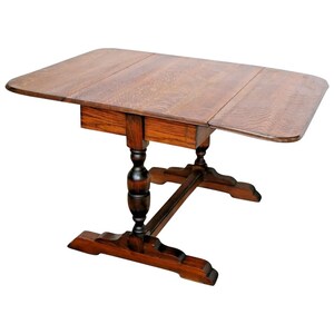 May include: A dark brown wooden drop leaf table with a single drawer and turned legs. The table has a rectangular top with two drop leaves that can be folded down.
